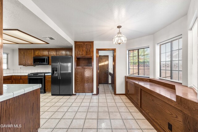 2613 W W Ave K4, Lancaster, CA 93536 - kitchen with stainless steel appliances, tile countertops, brown cabinetry, a chandelier, and light tile patterned flooring