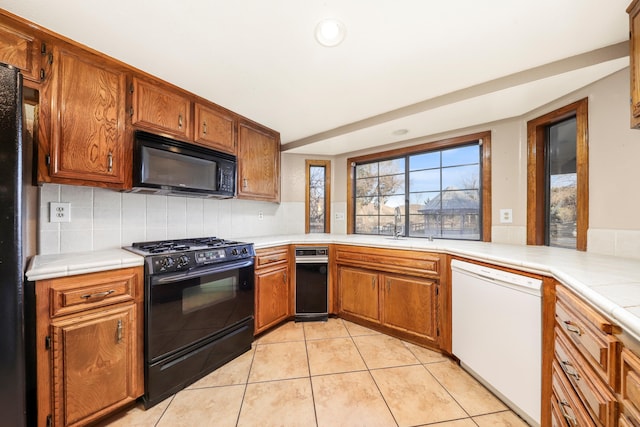 kitchen featuring kitchen peninsula, sink, tasteful backsplash, light tile patterned flooring, and black appliances