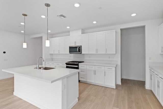 kitchen featuring visible vents, a sink, stainless steel microwave, light wood-style floors, and black range with gas stovetop