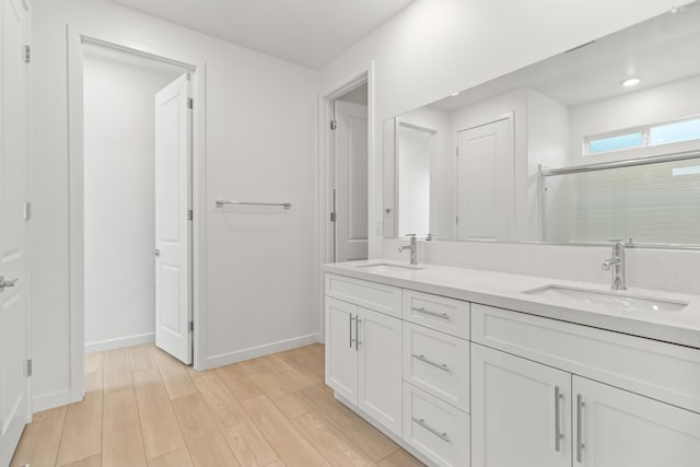 bathroom with a shower stall, wood finished floors, double vanity, and a sink