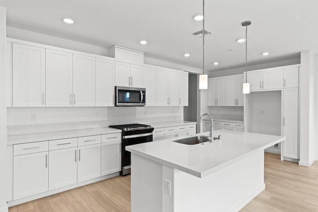 kitchen with gas stove, stainless steel microwave, white cabinetry, and a sink