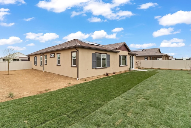 rear view of property featuring a yard, solar panels, a fenced backyard, and stucco siding