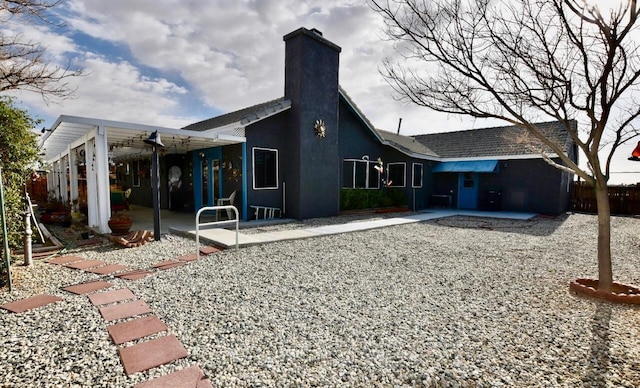 rear view of house featuring stucco siding, a chimney, and a patio