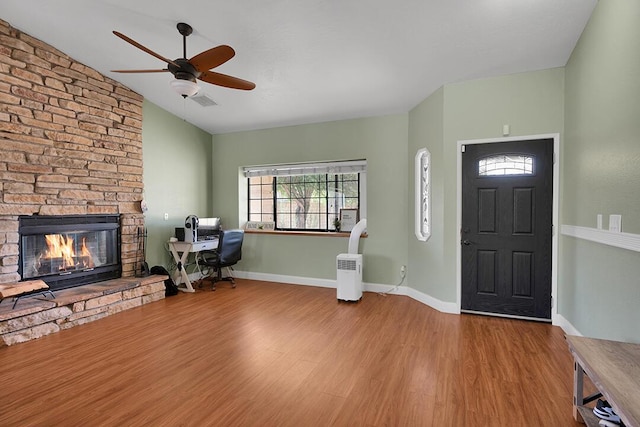 foyer entrance featuring hardwood / wood-style floors, a stone fireplace, ceiling fan, and lofted ceiling