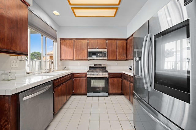 36933 Cadmia Ct, Palmdale, CA 93552 - kitchen with stainless steel appliances, a sink, light tile patterned floors, tile countertops, and brown cabinetry