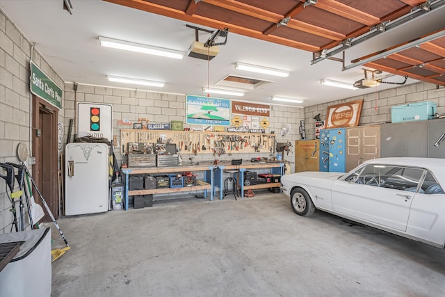 garage featuring a garage door opener, refrigerator, concrete block wall, and a workshop area