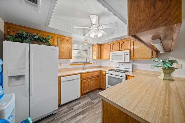 kitchen featuring light wood-type flooring, white appliances, a tray ceiling, ceiling fan, and sink