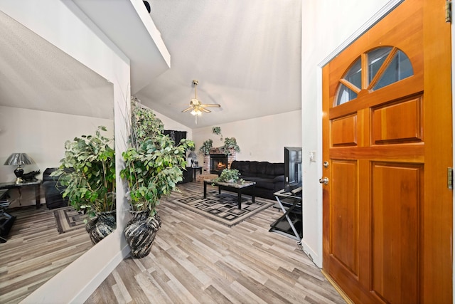 foyer entrance with ceiling fan, lofted ceiling, a fireplace, and light hardwood / wood-style flooring