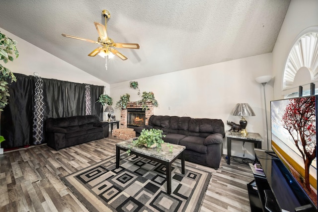 living room with a brick fireplace, a textured ceiling, ceiling fan, hardwood / wood-style floors, and lofted ceiling