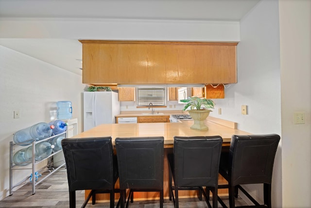 kitchen featuring white fridge with ice dispenser, sink, dark hardwood / wood-style flooring, kitchen peninsula, and a kitchen bar