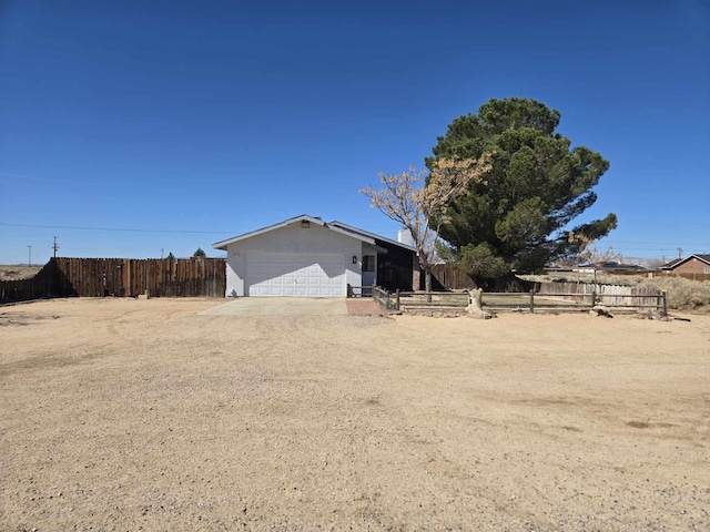 view of side of property featuring an attached garage, fence, and dirt driveway