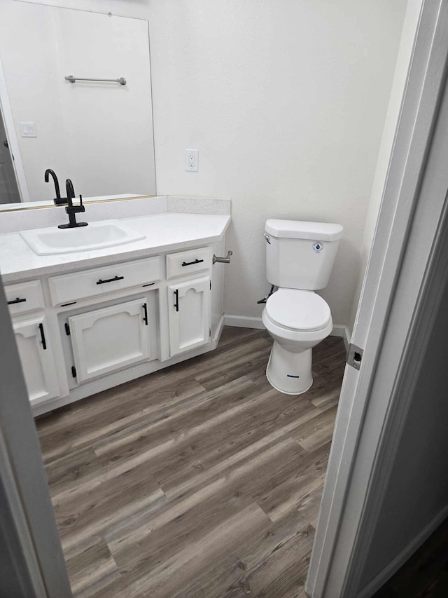 half bath featuring baseboards, toilet, wood finished floors, and vanity