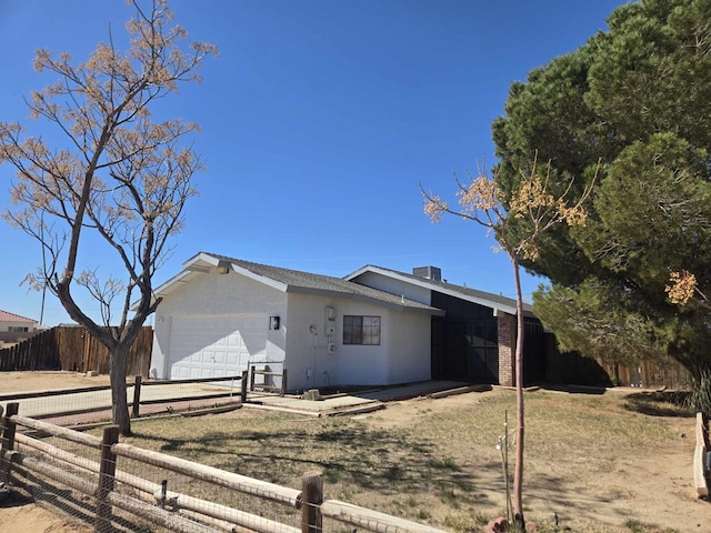 view of side of property featuring stucco siding, an attached garage, driveway, and fence