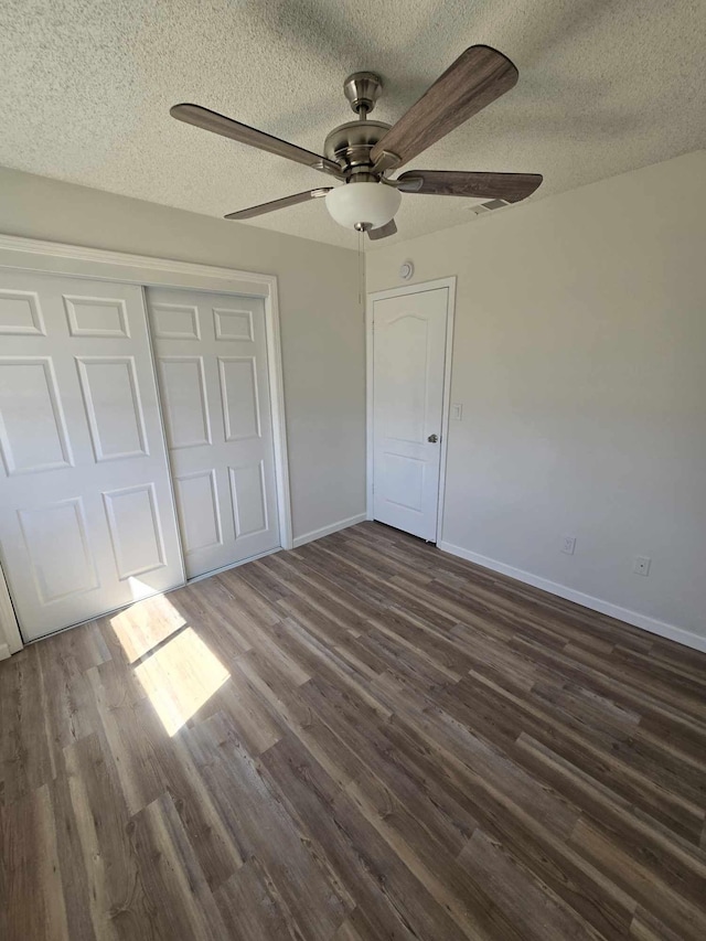 unfurnished bedroom with dark wood-style floors, a textured ceiling, baseboards, and a closet