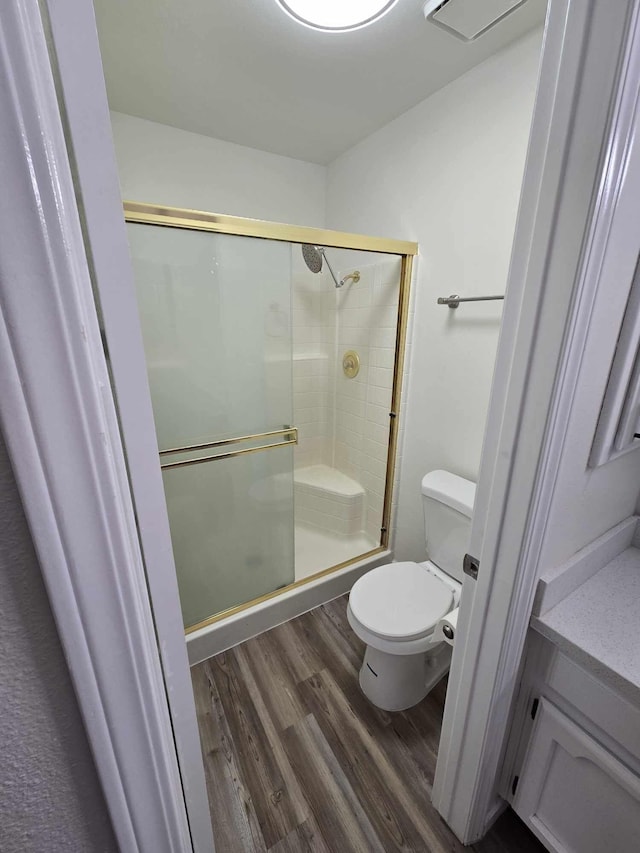 bathroom with a shower stall, toilet, and wood finished floors