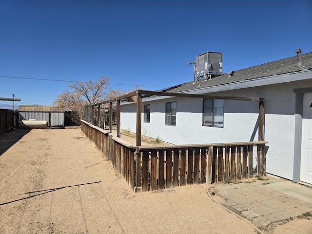 view of side of property featuring stucco siding, fence, cooling unit, and a shingled roof