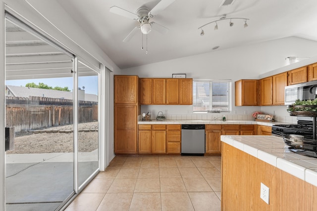 kitchen with stainless steel appliances, tile counters, vaulted ceiling, and a wealth of natural light