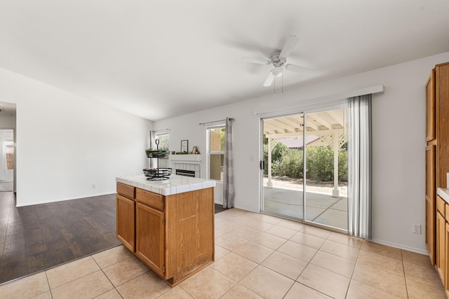 kitchen with light tile patterned flooring, baseboards, tile countertops, brown cabinets, and a ceiling fan