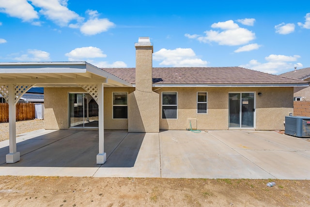 rear view of house featuring a chimney, a patio area, central air condition unit, fence, and stucco siding