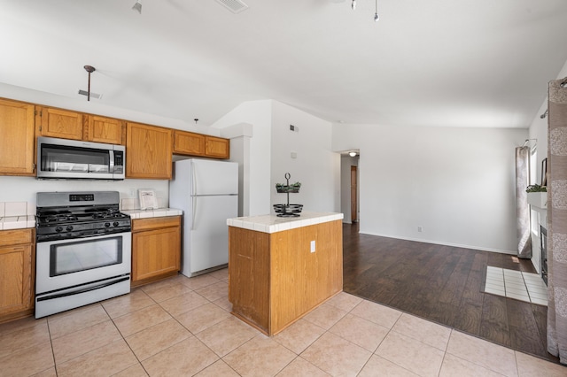 kitchen featuring a brick fireplace, light tile patterned flooring, tile countertops, brown cabinets, and stainless steel appliances