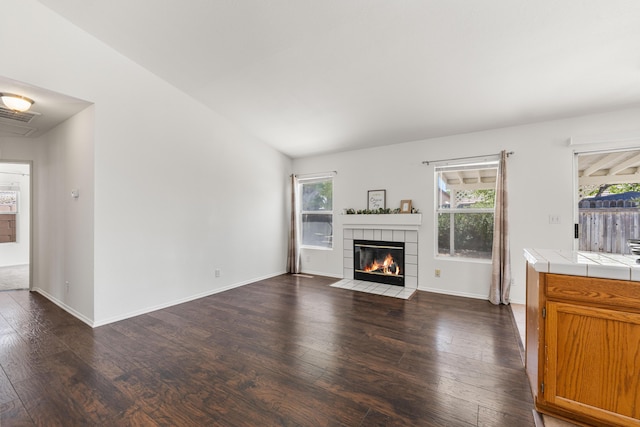 unfurnished living room with a healthy amount of sunlight, dark wood finished floors, a tile fireplace, and visible vents