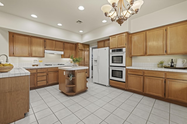 kitchen with tile countertops, hanging light fixtures, a kitchen island, a notable chandelier, and white appliances