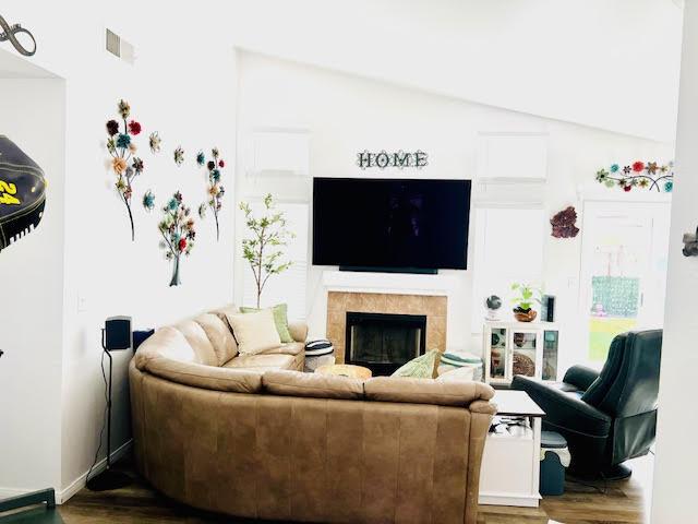 living room featuring a tiled fireplace, lofted ceiling, wood finished floors, and visible vents