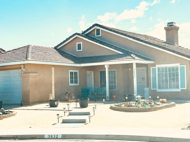 rear view of property with concrete driveway, a chimney, a garage, and stucco siding