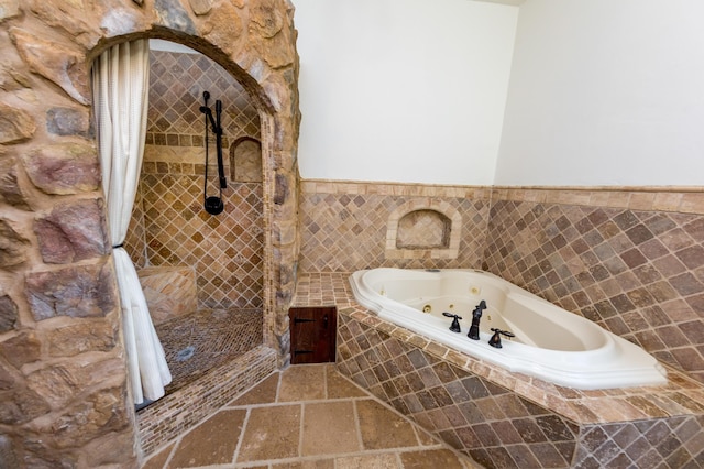bathroom featuring a wainscoted wall, a tub with jets, stone tile flooring, tile walls, and tiled shower