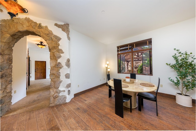 dining space featuring arched walkways, lofted ceiling, baseboards, and wood finished floors