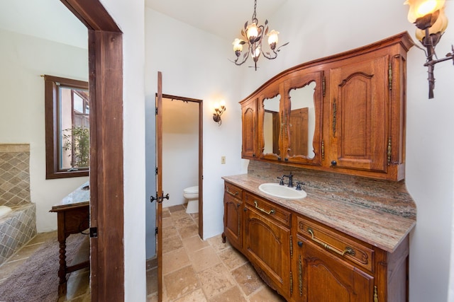 bathroom featuring stone tile floors, vanity, a chandelier, a relaxing tiled tub, and toilet
