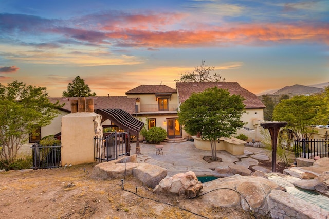back of house at dusk featuring stucco siding, fence, a patio, and a balcony