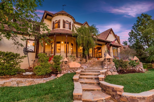 view of front facade featuring a front yard, covered porch, stairs, and stucco siding