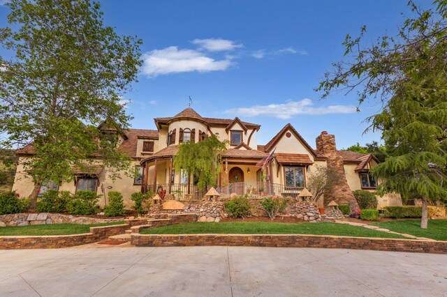 view of front of house featuring covered porch, a chimney, and stucco siding