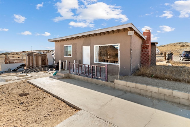 view of front of house with a chimney, fence, and stucco siding