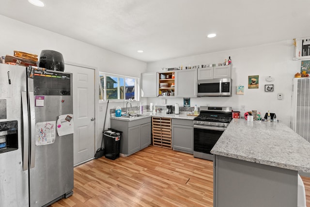 kitchen with kitchen peninsula, light wood-type flooring, gray cabinets, appliances with stainless steel finishes, and sink