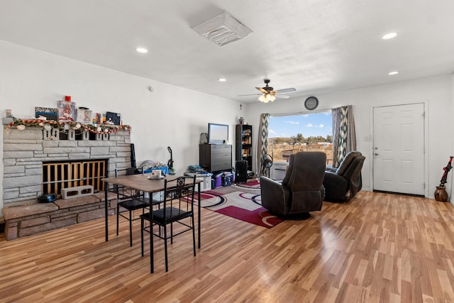 living room with a stone fireplace, light wood-type flooring, a ceiling fan, and recessed lighting