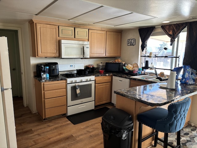 kitchen featuring wood-type flooring, sink, a breakfast bar area, kitchen peninsula, and white appliances