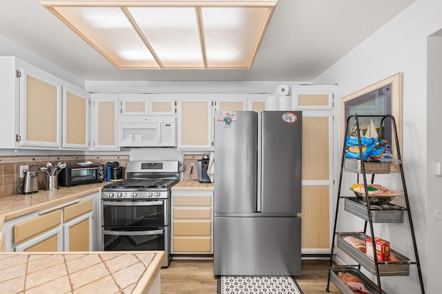 37940 E 42nd St Apt 115, Palmdale, CA 93552 - kitchen featuring stainless steel appliances, tile countertops, light wood-style flooring, white cabinetry, and glass insert cabinets