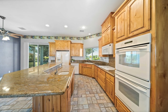 kitchen with stone countertops, a spacious island, white appliances, and sink