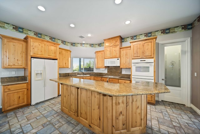 kitchen with light stone countertops, a center island, white appliances, and sink