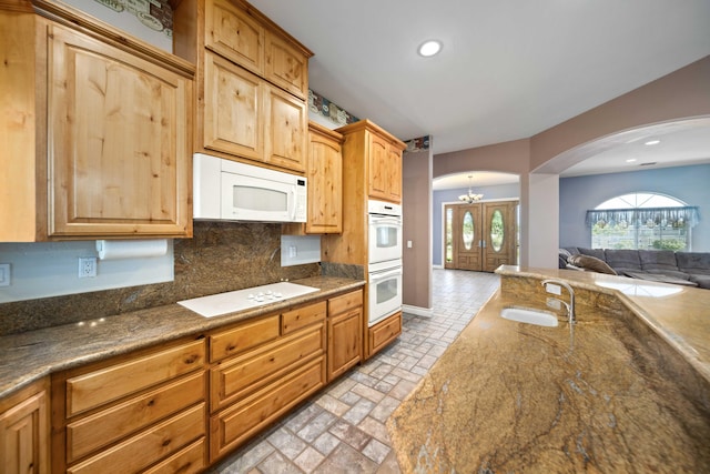 kitchen with sink, tasteful backsplash, a notable chandelier, dark stone counters, and white appliances