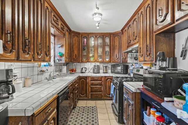 21104 Hillcrest Ct, Tehachapi, CA 93561 - kitchen with black appliances, under cabinet range hood, tile counters, tasteful backsplash, and light tile patterned floors