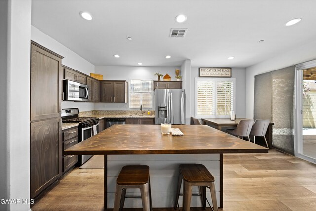 2038 Howard St, Rosamond, CA 93560 - kitchen with stainless steel appliances, dark brown cabinets, a breakfast bar, recessed lighting, and light wood-style floors