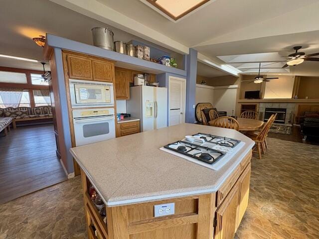 kitchen featuring a fireplace, lofted ceiling, a kitchen island, white appliances, and ceiling fan