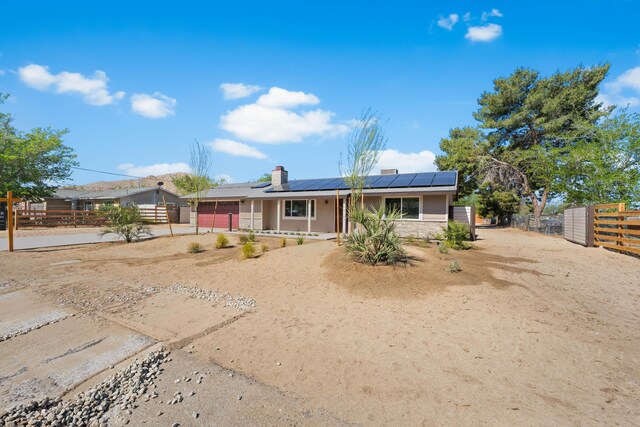 view of front of house featuring a chimney, solar panels, dirt driveway, fence, and an attached garage
