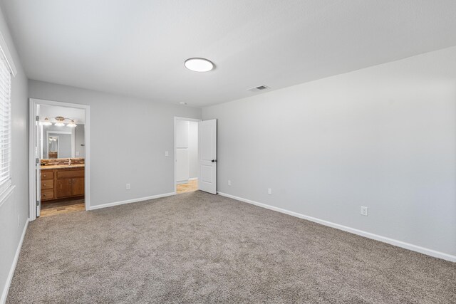 unfurnished bedroom featuring carpet flooring, connected bathroom, a sink, baseboards, and visible vents