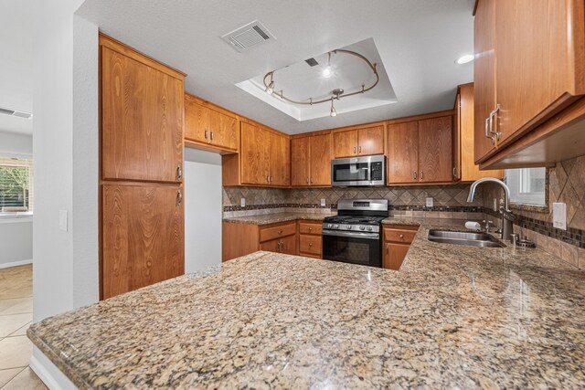 kitchen featuring visible vents, a raised ceiling, brown cabinets, a sink, and appliances with stainless steel finishes