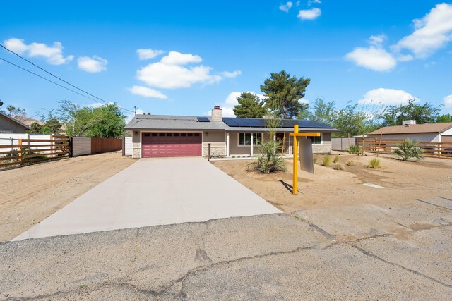 ranch-style home featuring an attached garage, roof mounted solar panels, fence, and concrete driveway