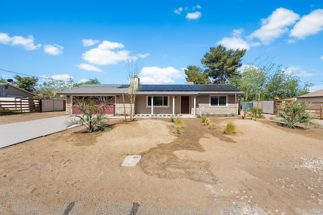 single story home with covered porch, solar panels, fence, concrete driveway, and stone siding